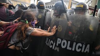 een jongeman in staartjes in Peru duwt tegen een rij politieagenten in oproeruitrusting